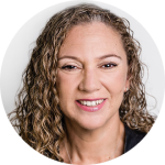 Portrait of a smiling woman with curly light brown hair against a neutral background.